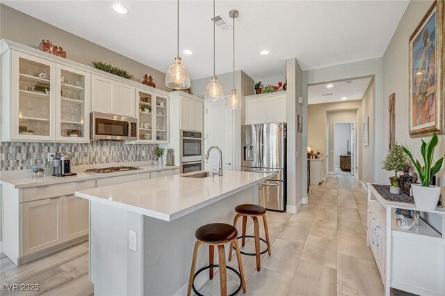 9940 Heather Moore Ave, Las Vegas, NV 89166 - kitchen featuring appliances with stainless steel finishes, a kitchen island with sink, backsplash, light countertops, and white cabinets