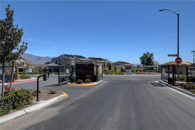 9940 Heather Moore Ave, Las Vegas, NV 89166 - view of asphalt road with curbs, a mountain view, a gated entry, street lighting, and a residential view