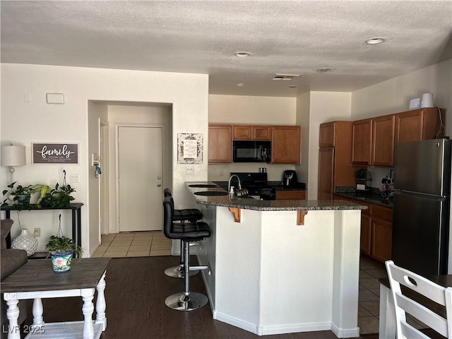 4013 Kindhearted Ct, North Las Vegas, NV 89032 - kitchen featuring black microwave, freestanding refrigerator, a kitchen bar, brown cabinetry, and dark stone counters