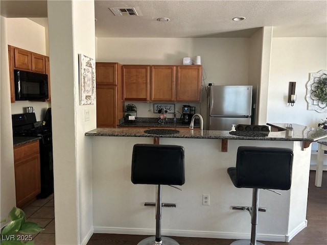 4013 Kindhearted Ct, North Las Vegas, NV 89032 - kitchen featuring black appliances, a breakfast bar, brown cabinetry, dark stone counters, and a textured ceiling