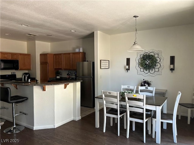 4013 Kindhearted Ct, North Las Vegas, NV 89032 - kitchen featuring black microwave, freestanding refrigerator, brown cabinets, a kitchen bar, and a textured ceiling