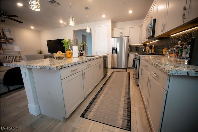 9584 Jadeite Ln, Las Vegas, NV 89143 - kitchen with appliances with stainless steel finishes, backsplash, a kitchen island with sink, hanging light fixtures, and light stone countertops