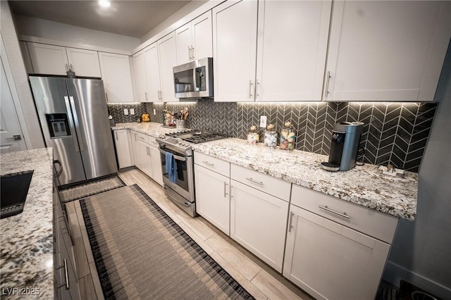 9584 Jadeite Ln, Las Vegas, NV 89143 - kitchen with appliances with stainless steel finishes, decorative backsplash, light stone countertops, and white cabinetry