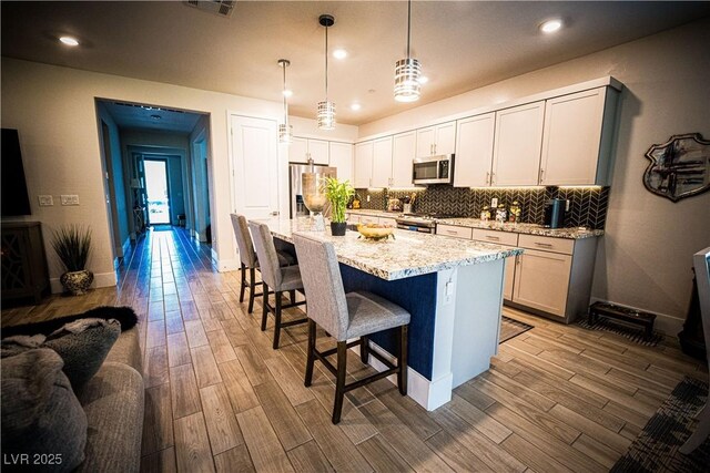 9584 Jadeite Ln, Las Vegas, NV 89143 - kitchen with stainless steel appliances, wood finished floors, backsplash, a kitchen breakfast bar, and light stone countertops
