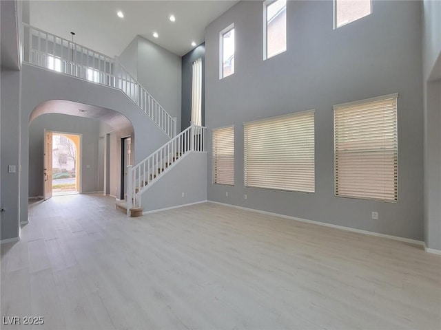 10482 Calico Pines Ave, Las Vegas, NV 89135 - unfurnished living room featuring arched walkways, a towering ceiling, stairs, wood finished floors, and recessed lighting