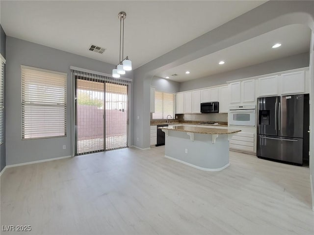 10482 Calico Pines Ave, Las Vegas, NV 89135 - kitchen with stainless steel fridge, black microwave, white oven, arched walkways, and white cabinetry