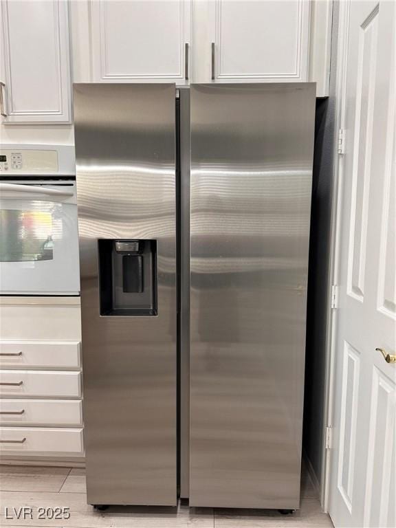 10482 Calico Pines Ave, Las Vegas, NV 89135 - detailed view of stainless steel fridge with ice dispenser, white oven, white cabinets, and light wood-style floors