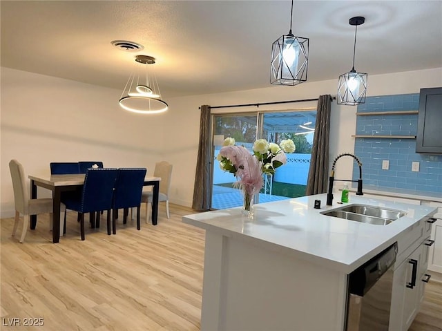 5321 Westleigh Ave, Las Vegas, NV 89146 - kitchen featuring stainless steel dishwasher, light countertops, light wood-style flooring, pendant lighting, and a center island with sink