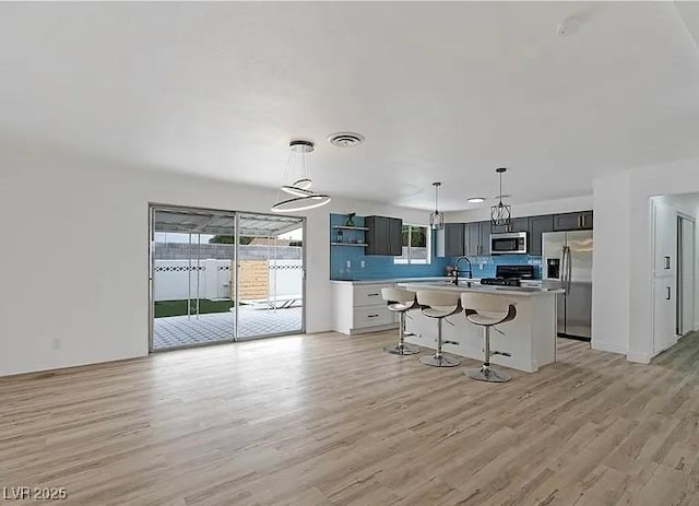 5321 Westleigh Ave, Las Vegas, NV 89146 - kitchen with appliances with stainless steel finishes, light wood-style floors, open shelves, a kitchen bar, and pendant lighting