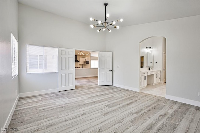 1002 Christopher View Ave, North Las Vegas, NV 89032 - spare room featuring a chandelier, arched walkways, light wood-style floors, and high vaulted ceiling