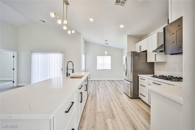 1002 Christopher View Ave, North Las Vegas, NV 89032 - kitchen with stainless steel appliances, vaulted ceiling, an island with sink, light wood finished floors, and white cabinetry