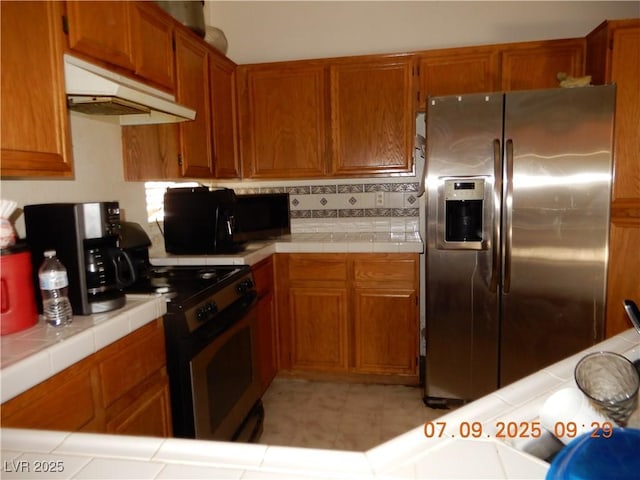 3428 Strawberry Roan Rd, North Las Vegas, NV 89032 - kitchen featuring appliances with stainless steel finishes, under cabinet range hood, tile countertops, brown cabinetry, and tasteful backsplash