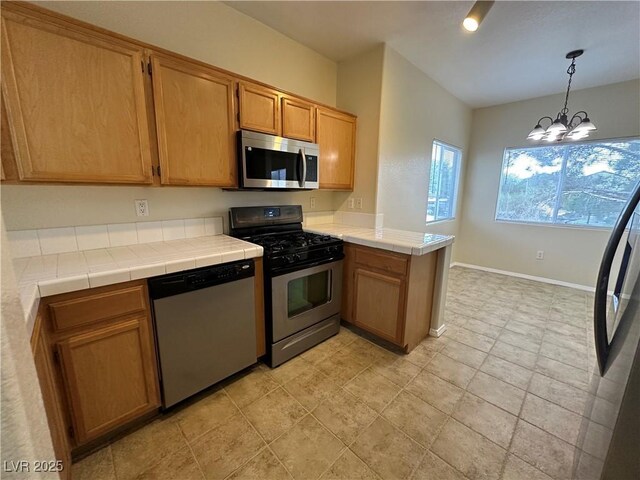 1050 E Cactus Ave Unit 2086, Las Vegas, NV 89183 - kitchen with stainless steel appliances, a peninsula, a chandelier, hanging light fixtures, and tile countertops
