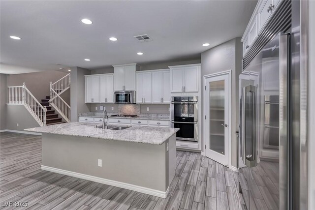 12313 Old Muirfield St, Las Vegas, NV 89141 - kitchen featuring appliances with stainless steel finishes, light wood-type flooring, white cabinets, recessed lighting, and an island with sink