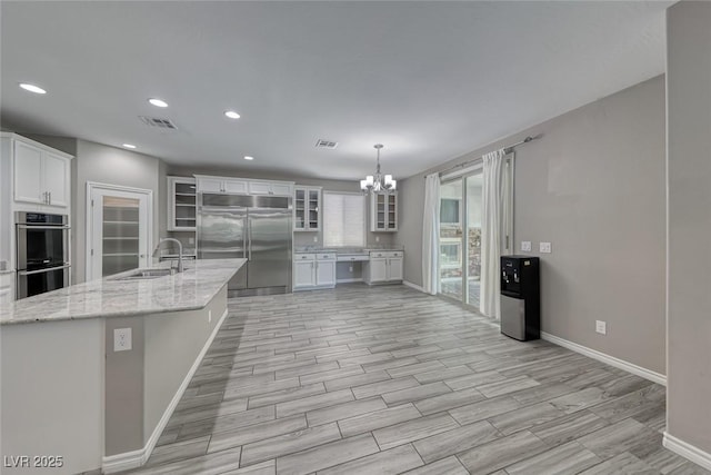12313 Old Muirfield St, Las Vegas, NV 89141 - kitchen featuring stainless steel appliances, a chandelier, white cabinetry, glass insert cabinets, and light stone counters