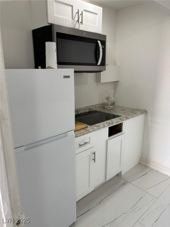 3361 Horizon St, Las Vegas, NV 89121 - kitchen with freestanding refrigerator, stainless steel microwave, black electric cooktop, white cabinets, and light marble finish floors