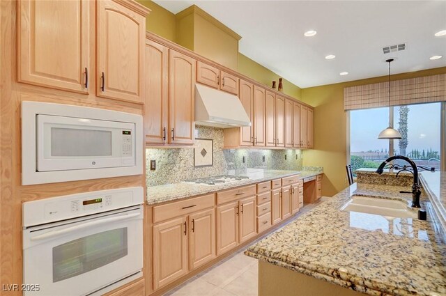 212 Florio Ct, Las Vegas, NV 89138 - kitchen featuring white appliances, light brown cabinetry, under cabinet range hood, light stone counters, and backsplash