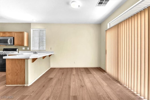 9948 Trailing Vine St, Las Vegas, NV 89183 - kitchen featuring stainless steel microwave, white range with gas stovetop, light wood-type flooring, a kitchen bar, and plenty of natural light