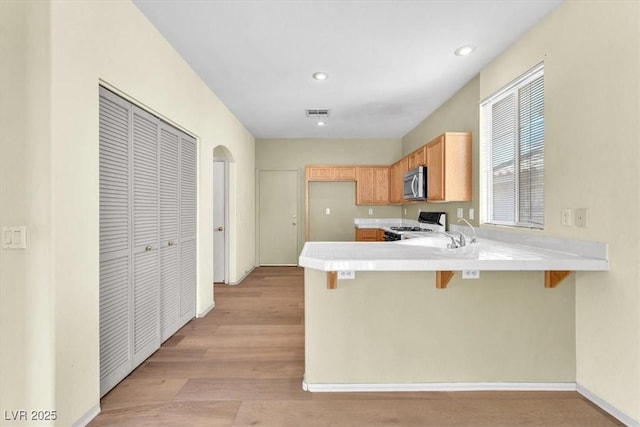9948 Trailing Vine St, Las Vegas, NV 89183 - kitchen featuring stainless steel microwave, range, a peninsula, a kitchen breakfast bar, and light wood-style floors