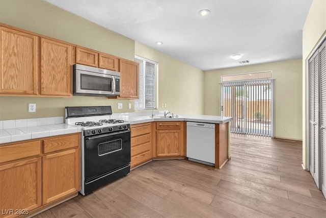 9948 Trailing Vine St, Las Vegas, NV 89183 - kitchen featuring white dishwasher, stainless steel microwave, gas range, a peninsula, and light wood-style flooring