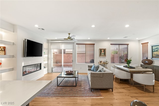 2310 Malaga Peak St, Las Vegas, NV 89135 - living room featuring a ceiling fan, light wood-type flooring, a glass covered fireplace, and recessed lighting