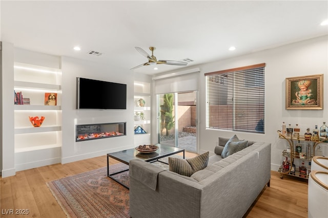 2310 Malaga Peak St, Las Vegas, NV 89135 - living area with a glass covered fireplace, a ceiling fan, light wood-style flooring, recessed lighting, and built in shelves