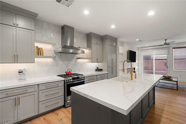 2310 Malaga Peak St, Las Vegas, NV 89135 - kitchen featuring stainless steel gas range oven, wall chimney exhaust hood, gray cabinets, a ceiling fan, and light stone counters