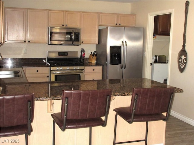 10013 Solid Lime St, Las Vegas, NV 89183 - kitchen with stainless steel appliances, wood finished floors, a peninsula, a breakfast bar area, and dark stone countertops