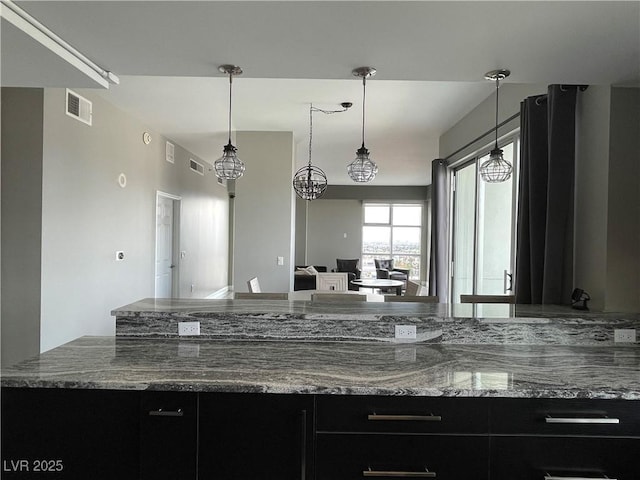 150 Las Vegas Blvd Unit 1115, Las Vegas, NV 89101 - kitchen featuring dark cabinetry, stone counters, open floor plan, and hanging light fixtures
