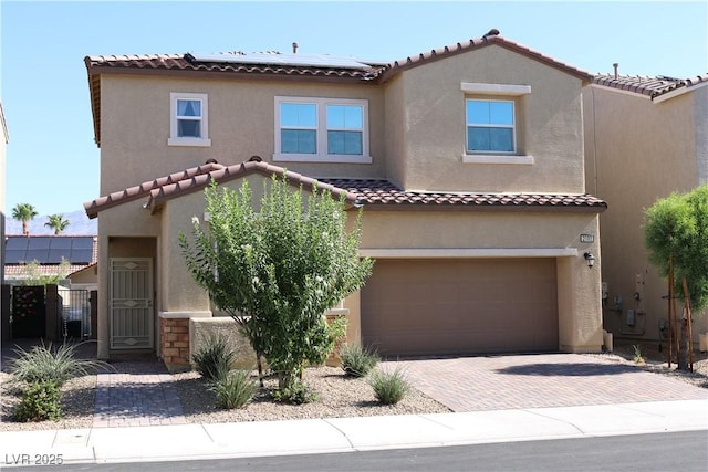 2102 Stone Well Rd, North Las Vegas, NV 89031 - mediterranean / spanish-style house featuring an attached garage, stucco siding, solar panels, a tile roof, and decorative driveway