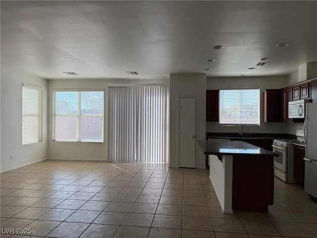 5905 Addy Ln, North Las Vegas, NV 89081 - kitchen with white appliances, dark countertops, a kitchen island, open floor plan, and light tile patterned flooring