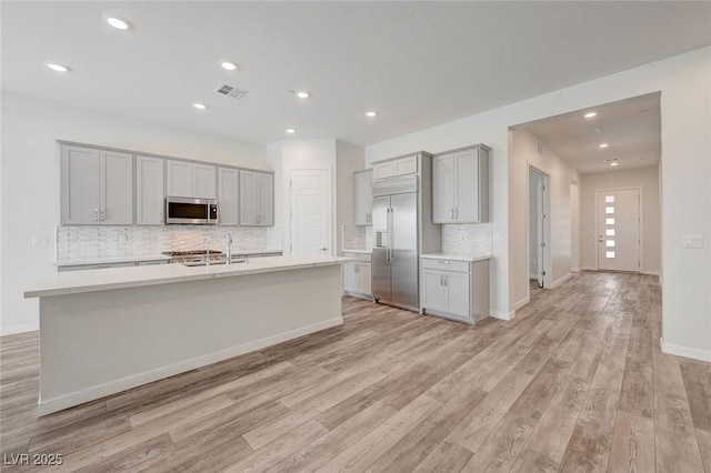 12436 Primrose Grove Ln, Las Vegas, NV 89138 - kitchen with stainless steel appliances, gray cabinets, tasteful backsplash, light wood-type flooring, and a kitchen island with sink