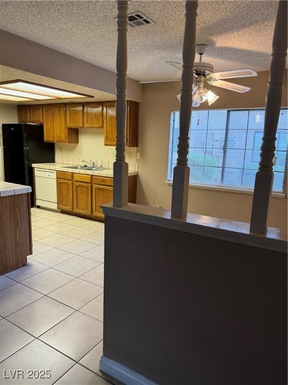 4231 Sanderling Cir Unit 267, Las Vegas, NV 89103 - kitchen with white dishwasher, ceiling fan, brown cabinets, light tile patterned floors, and a textured ceiling