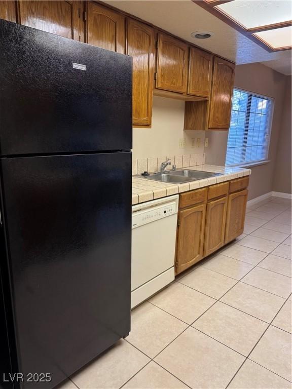 4231 Sanderling Cir Unit 267, Las Vegas, NV 89103 - kitchen featuring freestanding refrigerator, dishwasher, tile counters, light tile patterned floors, and brown cabinets
