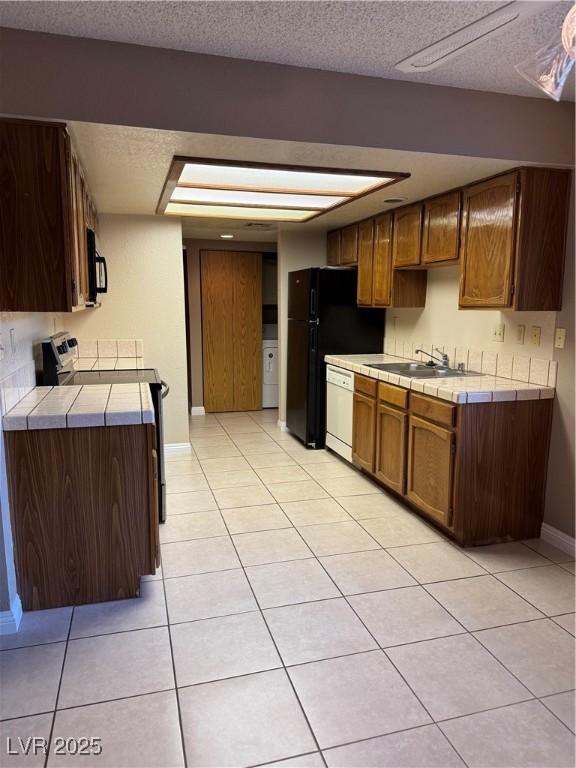 4231 Sanderling Cir Unit 267, Las Vegas, NV 89103 - kitchen with black appliances, tile countertops, light tile patterned floors, a textured ceiling, and washer / dryer