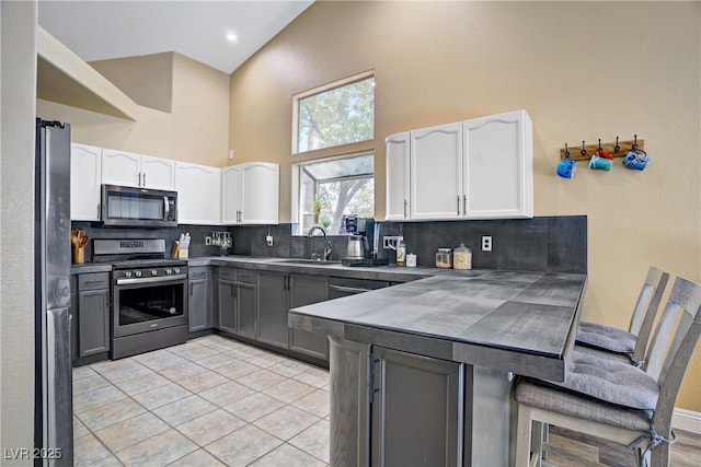 7401 Red Swallow St, Las Vegas, NV 89131 - kitchen with appliances with stainless steel finishes, a towering ceiling, gray cabinetry, a peninsula, and tasteful backsplash