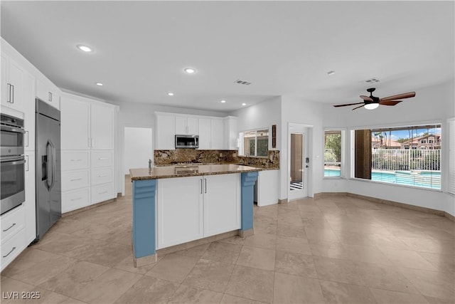 56 Grossinger Ct, Henderson, NV 89074 - kitchen featuring appliances with stainless steel finishes, decorative backsplash, dark stone counters, white cabinetry, and ceiling fan