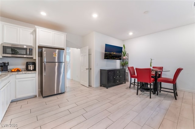 7107 Calvert Cliffs St, North Las Vegas, NV 89084 - kitchen with stainless steel appliances, white cabinetry, light stone counters, light wood-type flooring, and recessed lighting