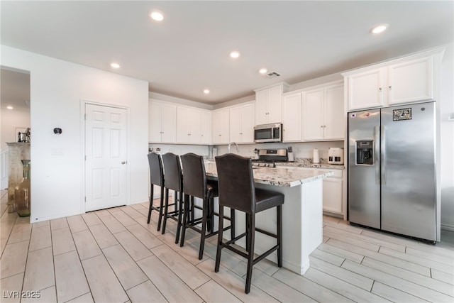 7107 Calvert Cliffs St, North Las Vegas, NV 89084 - kitchen with appliances with stainless steel finishes, white cabinets, a kitchen breakfast bar, wood finish floors, and an island with sink