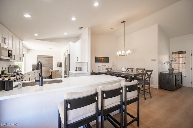 2548 Tumble Brook Dr, Las Vegas, NV 89134 - kitchen with stainless steel appliances, white cabinets, light wood-style floors, a peninsula, and a breakfast bar area
