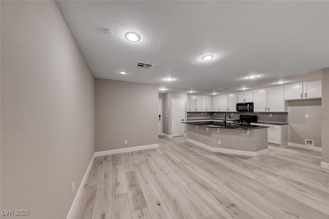 2337 Via Barranca St, Henderson, NV 89044 - kitchen featuring dark countertops, white cabinetry, light wood finished floors, backsplash, and black microwave