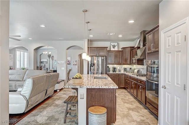 3605 Greenbriar Bluff Ave, North Las Vegas, NV 89081 - kitchen with arched walkways, stainless steel appliances, open floor plan, a kitchen breakfast bar, and light stone counters