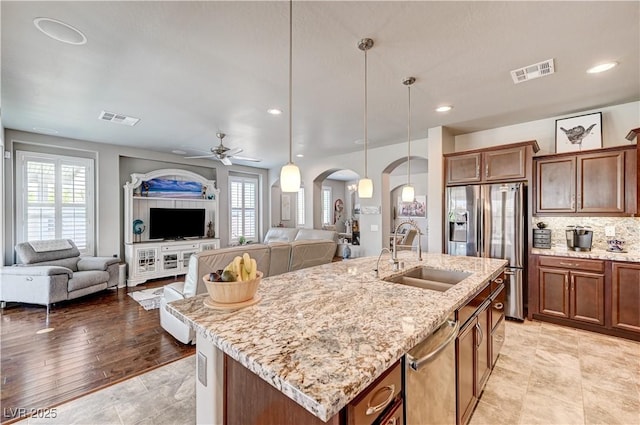 3605 Greenbriar Bluff Ave, North Las Vegas, NV 89081 - kitchen featuring arched walkways, stainless steel appliances, open floor plan, a center island with sink, and light stone countertops