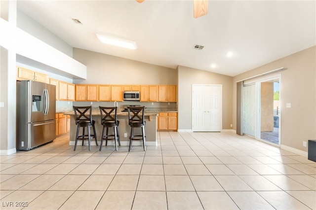 1442 Big Tree Ave, North Las Vegas, NV 89031 - kitchen featuring stainless steel appliances, light brown cabinetry, lofted ceiling, a kitchen breakfast bar, and a center island
