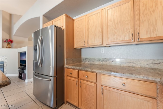 1442 Big Tree Ave, North Las Vegas, NV 89031 - kitchen featuring stainless steel fridge with ice dispenser, light brown cabinets, light tile patterned floors, light stone counters, and arched walkways