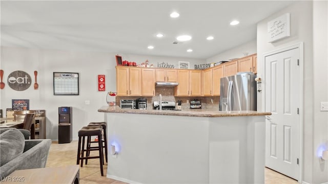 7723 Widewing Dr, North Las Vegas, NV 89084 - kitchen with stainless steel fridge, light brown cabinets, under cabinet range hood, decorative backsplash, and light tile patterned floors