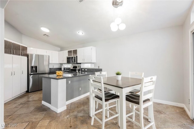 2547 Sundew Ave, Henderson, NV 89052 - kitchen with dark countertops, stainless steel appliances, lofted ceiling, light stone finish floors, and white cabinetry