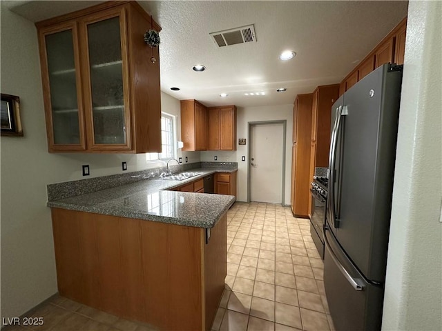 5449 Bugle Way Unit 105, Las Vegas, NV 89108 - kitchen featuring freestanding refrigerator, brown cabinets, a peninsula, black gas range oven, and glass insert cabinets