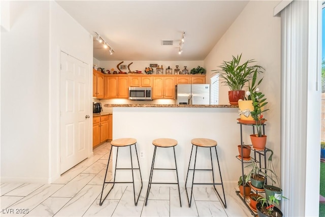 6312 Beige Bluff St Unit 102, North Las Vegas, NV 89081 - kitchen featuring stainless steel appliances, light marble finish floors, a breakfast bar area, rail lighting, and a peninsula