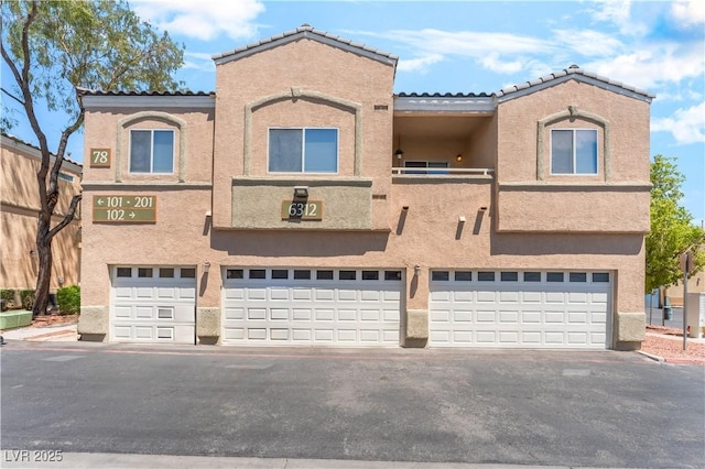 6312 Beige Bluff St Unit 102, North Las Vegas, NV 89081 - view of property featuring an attached garage, stucco siding, asphalt driveway, and a tile roof